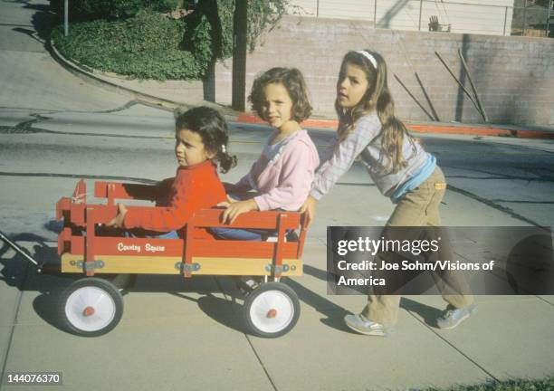 Three girls playing with a red wagon in Glendale, CA