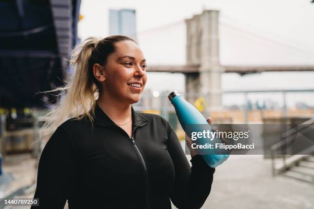 a young adult woman is doing a break during a fitness session in the city - buxom blonde stock pictures, royalty-free photos & images