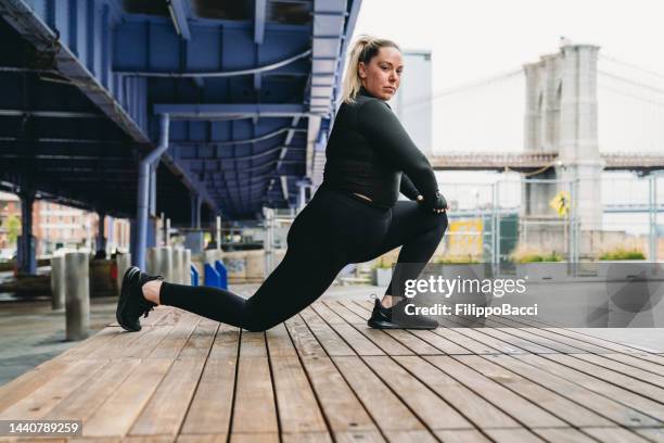 a young adult woman is training in the city, doing stretching in lower manhattan - buxom blonde stock pictures, royalty-free photos & images