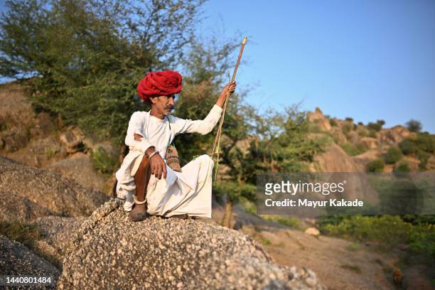 portrait of a senior rabari shepherd man, sitting with his guarding stick on a rock - nomad cattle herder from rajasthan stock-fotos und bilder
