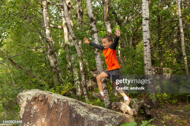 niño saltando de tronco a roca en el bosque - tronco fotografías e imágenes de stock