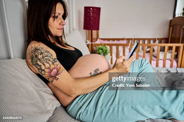 pregnant in bed surfing the internet - maternity wear photos et images de collection
