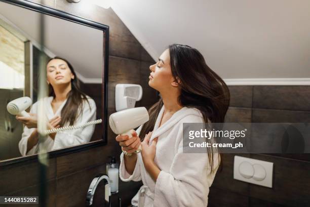 バスローブを着てバスルームで髪を乾かす若い女性 - hair dryer ストックフォトと画像
