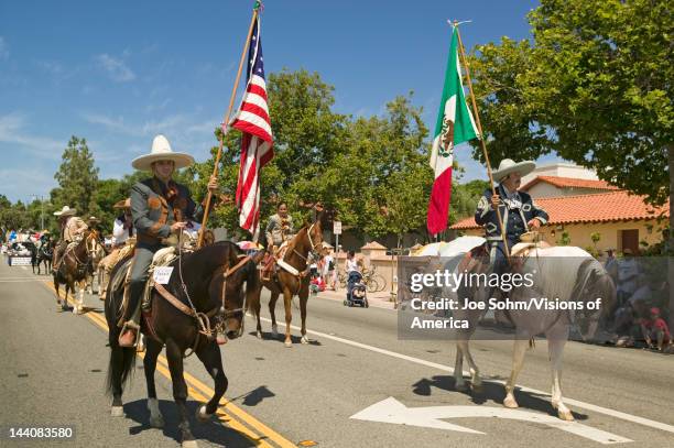 Parade participants on horseback carrying American and Mexican flags make their way down main street during a Fourth of July parade in Ojai, CA