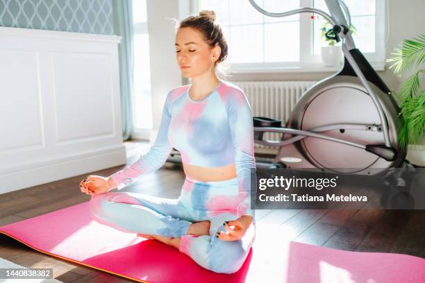 calm woman sit in lotus pose, practicing yoga meditation on pink yoga mat on the floor in light room indoors - self discipline imagens e fotografias de stock