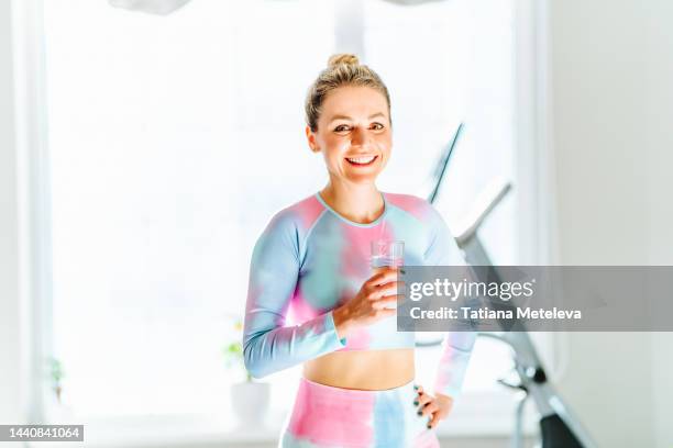 athletic slim body and healthy lifestyle with glass of water. cheerful blond athlete woman drinking water during sport exercises in gym or sports class - athlete bulges stock pictures, royalty-free photos & images