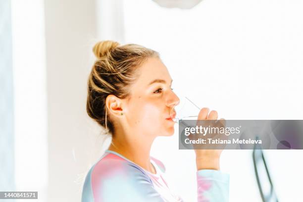 body care, recovery with isotonic drink. sportswoman drinking water from glass against light window. profile view - water close up stock pictures, royalty-free photos & images