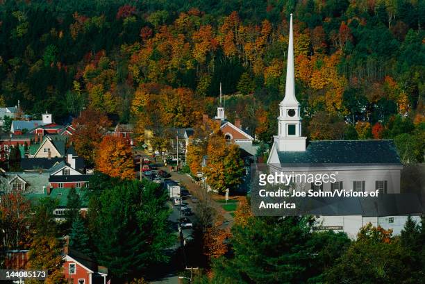 This is Scenic Route 100 in the autumn, There is a large white New England style church with a tall steeple next to smaller buildings of the town,