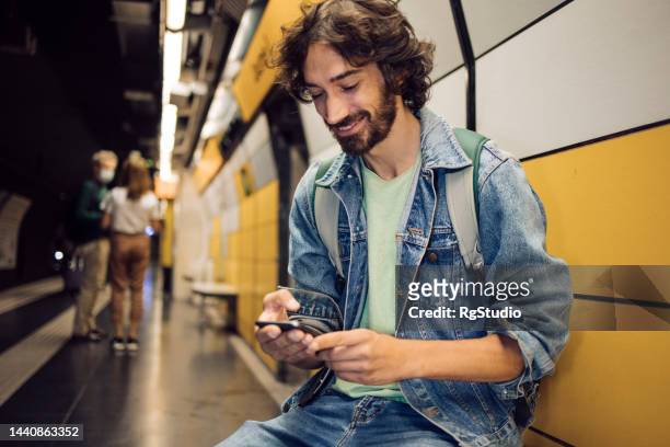 young tourist waiting for his subway train and using smartphone - spanish and portuguese ethnicity stock pictures, royalty-free photos & images