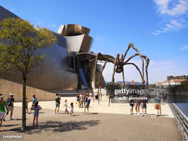 tourists at guggenheim museum on the riverbank in bilbao, spain - guggenheim museum bilbao stockfoto's en -beelden