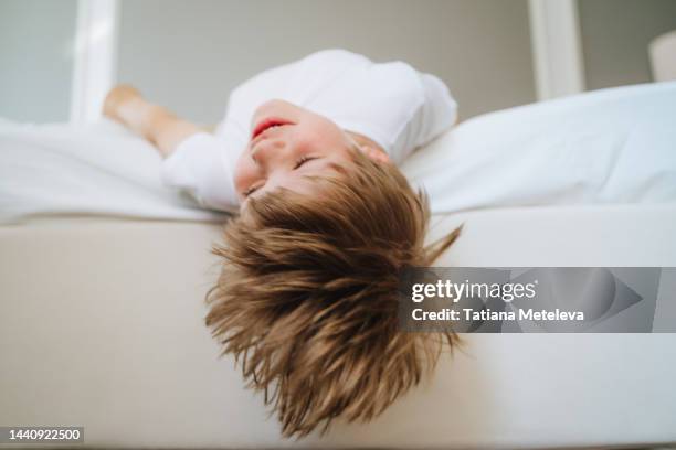 hair care, child dandruff. close up of boy upside down face laughing and having fun on white bed - caspa - fotografias e filmes do acervo