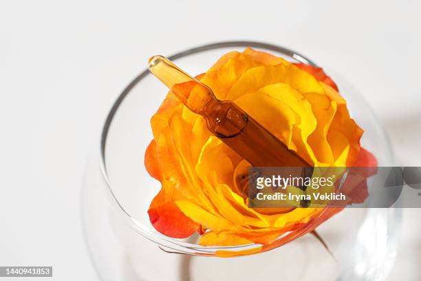 glass ampoule of the  cosmetic product with natural origin hyaluronic acid and vitamin c and tea rose on a white background. - white rose flower spa stock-fotos und bilder