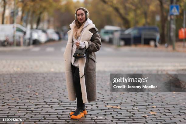 Sonia Lyson seen wearing Bottega Veneta black and neon orange leather boots, H&M black leggings, a Balenciaga white logo sweater, a Balenciaga...