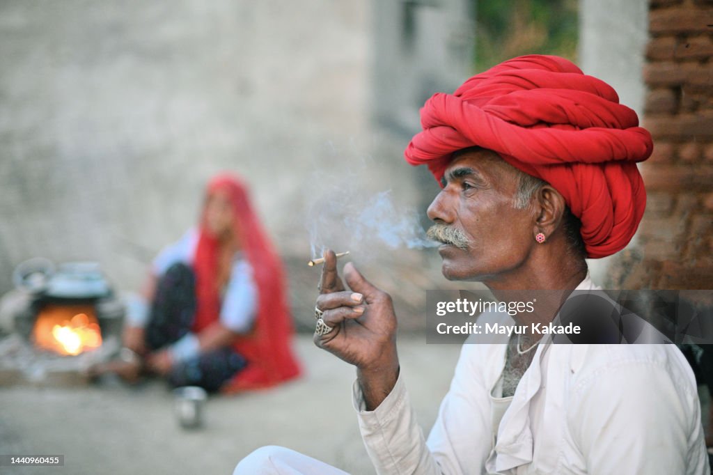 Side view of a Senior Rabari man smoking a beedi sitting outdoor wearing a red turban