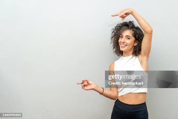 smiling curly haired woman pointing finger at blank wall. - woman index finger stock pictures, royalty-free photos & images