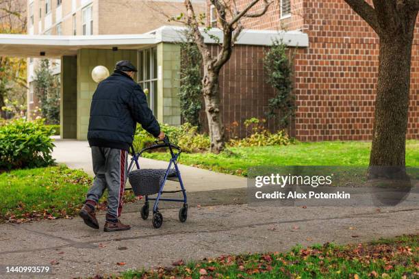 un hombre de 98 años camina por la calle con un andador en otoño. - viviendas asequibles fotografías e imágenes de stock