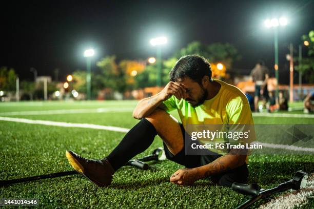 worried mid adult amputee soccer player sitting on soccer field - injured football player stock pictures, royalty-free photos & images