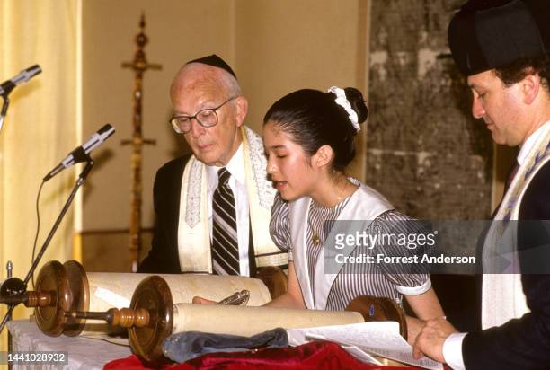 Watched by a pair of rabbis, an unidentified girl reads from the Torah during her Bat Mitzvah, Kaifeng, China, 1990.