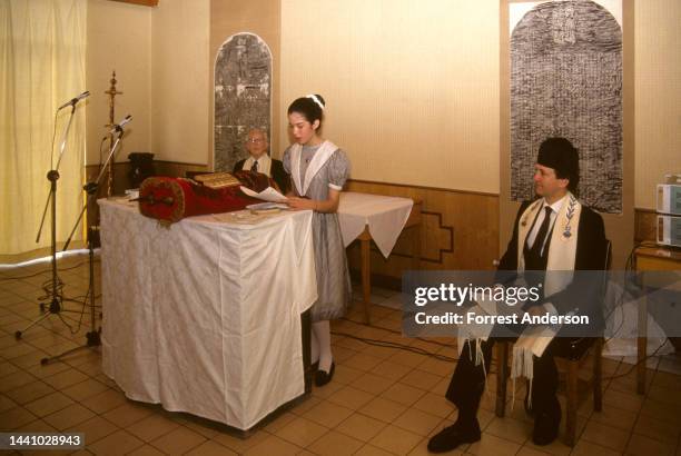 Watched by a pair of rabbis, an unidentified girl reads from the Torah during her Bat Mitzvah, Kaifeng, China, 1990.