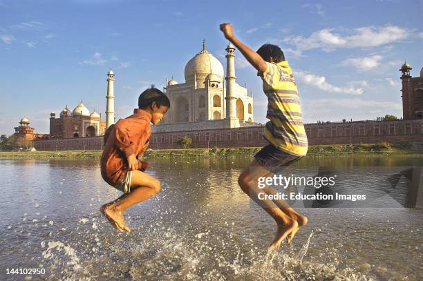 Two Children Playing In The Water Of River Yamuna Flowing Besides The Taj Mahal , Agra, Delhi, India.