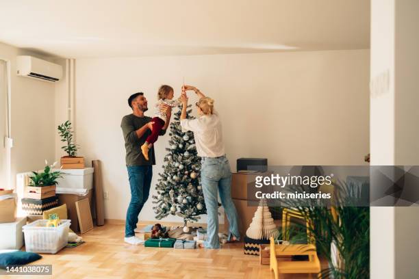happy family decorating christmas tree in new home - homeowners decorate their houses for christmas stockfoto's en -beelden
