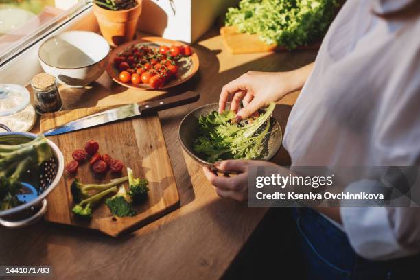 healthy dinner or lunch. woman in t-shirt and jeans standing and holding vegan superbowl or buddha bowl with hummus, vegetable, salad, beans, couscous and avocado and smoothie in hands, square crop - kreuzblütengewächse stock-fotos und bilder