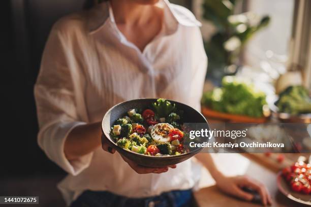 healthy dinner or lunch. woman in t-shirt and jeans standing and holding vegan superbowl or buddha bowl with hummus, vegetable, salad, beans, couscous and avocado and smoothie in hands, square crop - porzione di cibo foto e immagini stock