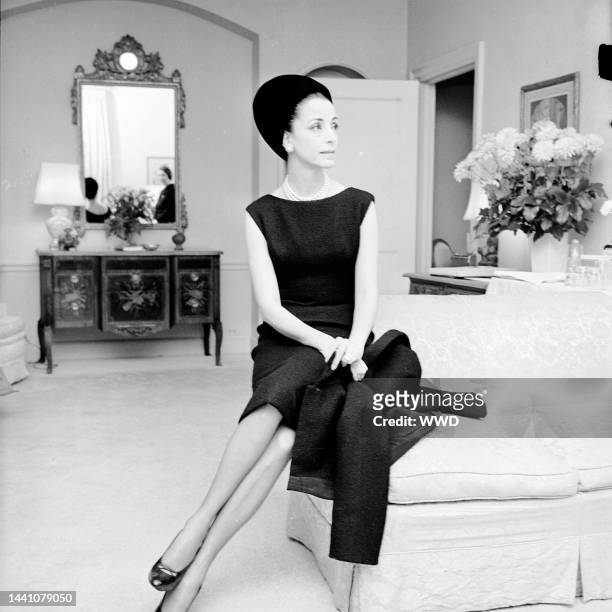 Outtake; Gloria Guinness seated in her suite at the Waldorf Towers wearing a black wool Givenchy jacket bordered in black faille over a sleeveless...