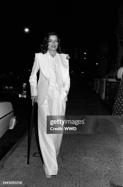 Bianca Jagger arrives for a party thrown by Kenny Lane in a Murray Hill area townhouse. Jagger wears a white Halston suit and walks with a cane