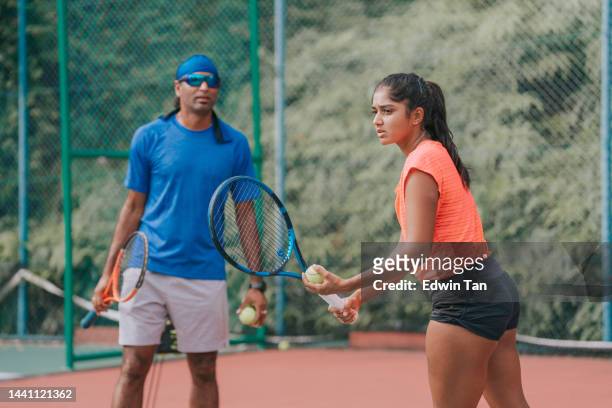 sport training asian indian female tennis player serving the ball practicing at tennis court with coach guidance - hardcourt stock pictures, royalty-free photos & images