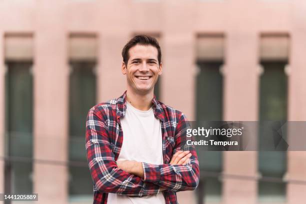 portrait of a happy young hipster guy walking in the city while chatting on his cellphone - mh stock pictures, royalty-free photos & images