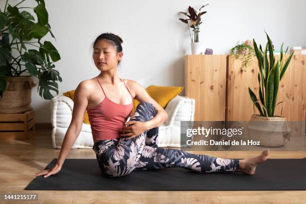 young asian woman doing yoga at home. doing seated spinal twist at home living room. - seated spinal twist stock pictures, royalty-free photos & images