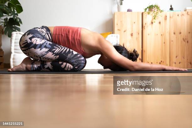 young asian woman doing childs pose on yoga mat at home living room. - dorsal fin stock photos et images de collection