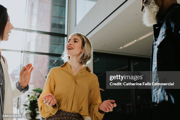 a woman has a lighthearted discussion with two people - she is animated as she gestures with her hands - beförderung arbeit stock-fotos und bilder