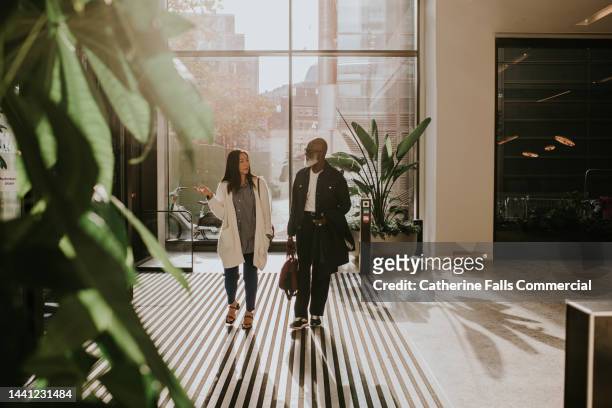 a woman and a man enter a modern building and look around with curiosity - enterprise stock pictures, royalty-free photos & images