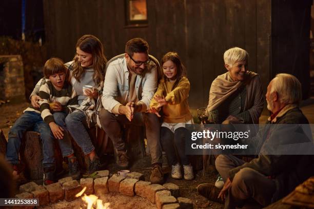 família feliz e estendida curtindo pela fogueira à noite. - chalet - fotografias e filmes do acervo