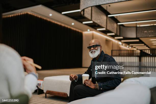 a man is the focus, sitting with a woman on a large white sofa in a large modern environment. - casual job interview stock pictures, royalty-free photos & images