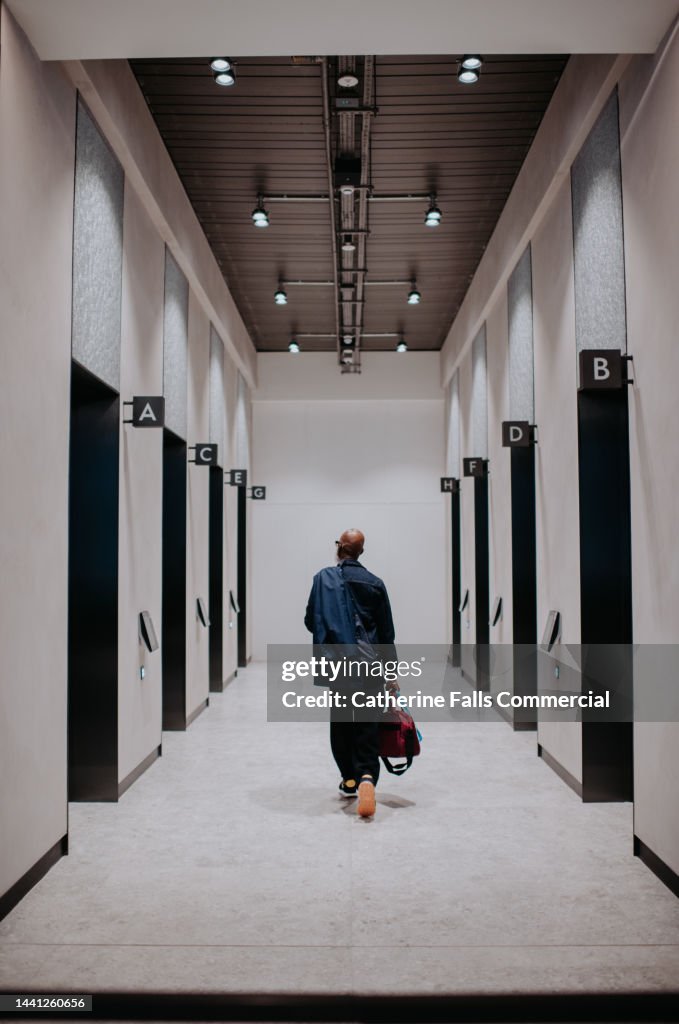 A man walks towards a elevator through a hallway