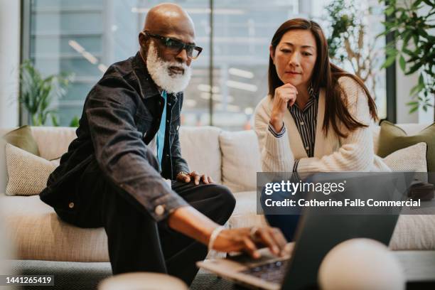 a man and a woman on a stylish white sofa in a contemporary office building have a casual business meeting - réunion du personnel photos et images de collection
