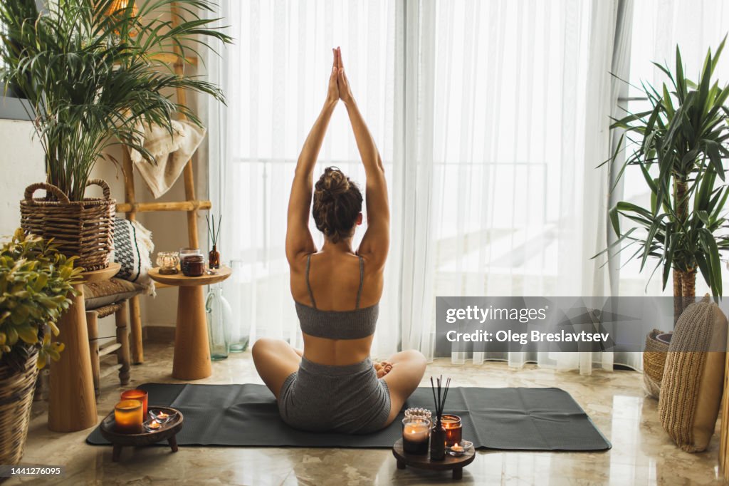 View from behind of woman meditating and practicing yoga alone at home in morning