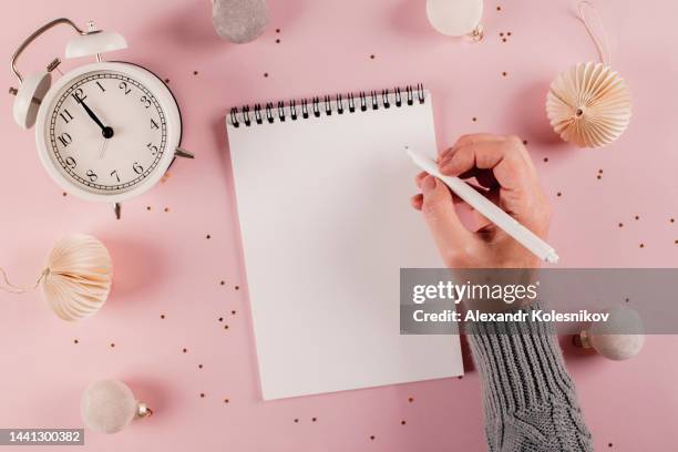 female hand writing plans, goals in white note pad on pink background. directly above - new year's day stockfoto's en -beelden