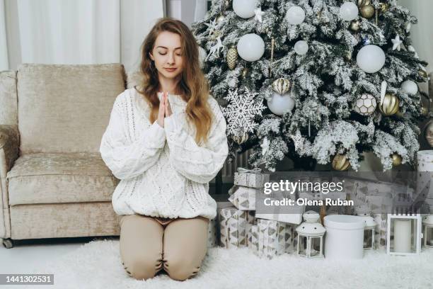 young woman folding hands in namaste against xmas tree. - prayer pose greeting fotografías e imágenes de stock