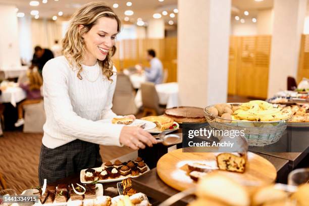 woman choosing breakfast from buffet table at the hotel restaurant - buffet stockfoto's en -beelden