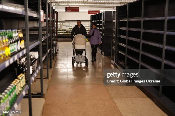 Couple with baby carriage walk past empty shelves in the supermarket on November 13, 2022 in Kherson, Ukraine. A curfew was introduced in the city...