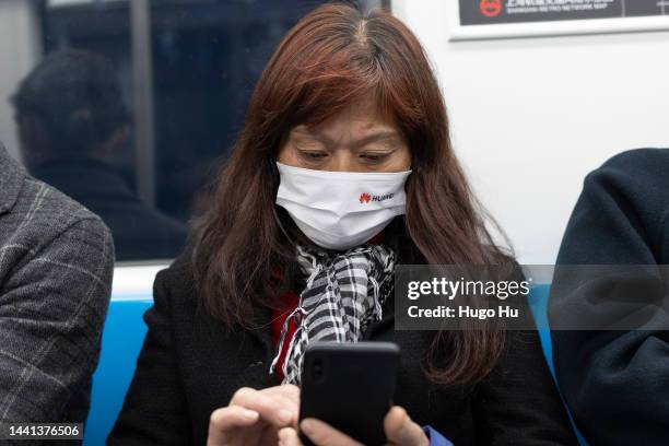 Woman with a protective mask with a HUAWEI logo looks at her smartphone in a subway car on November 14, 2022 in Shanghai, China.