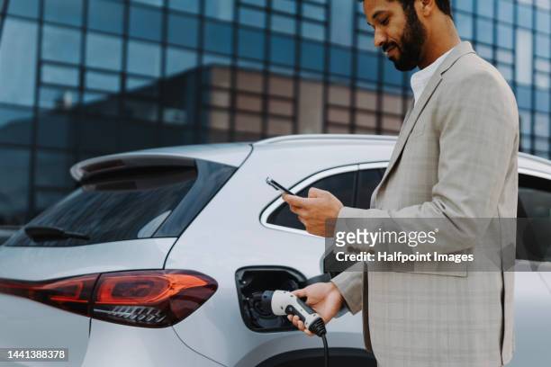 young multiracial businessman charging his car. - battery charger 個照片及圖片檔