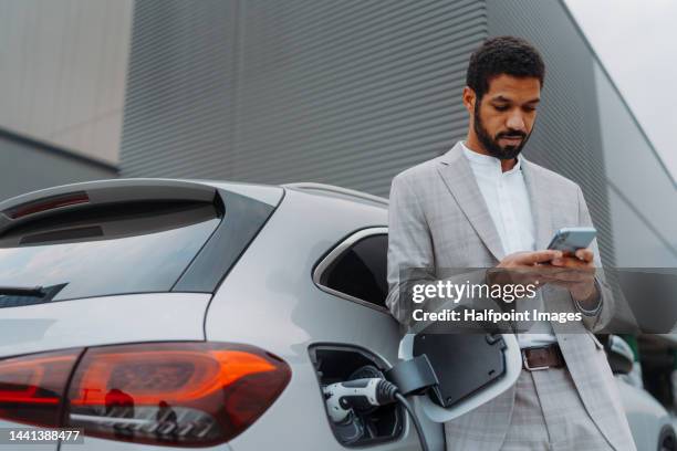 young multiracial man waiting for car charging. - elektro auto stock-fotos und bilder