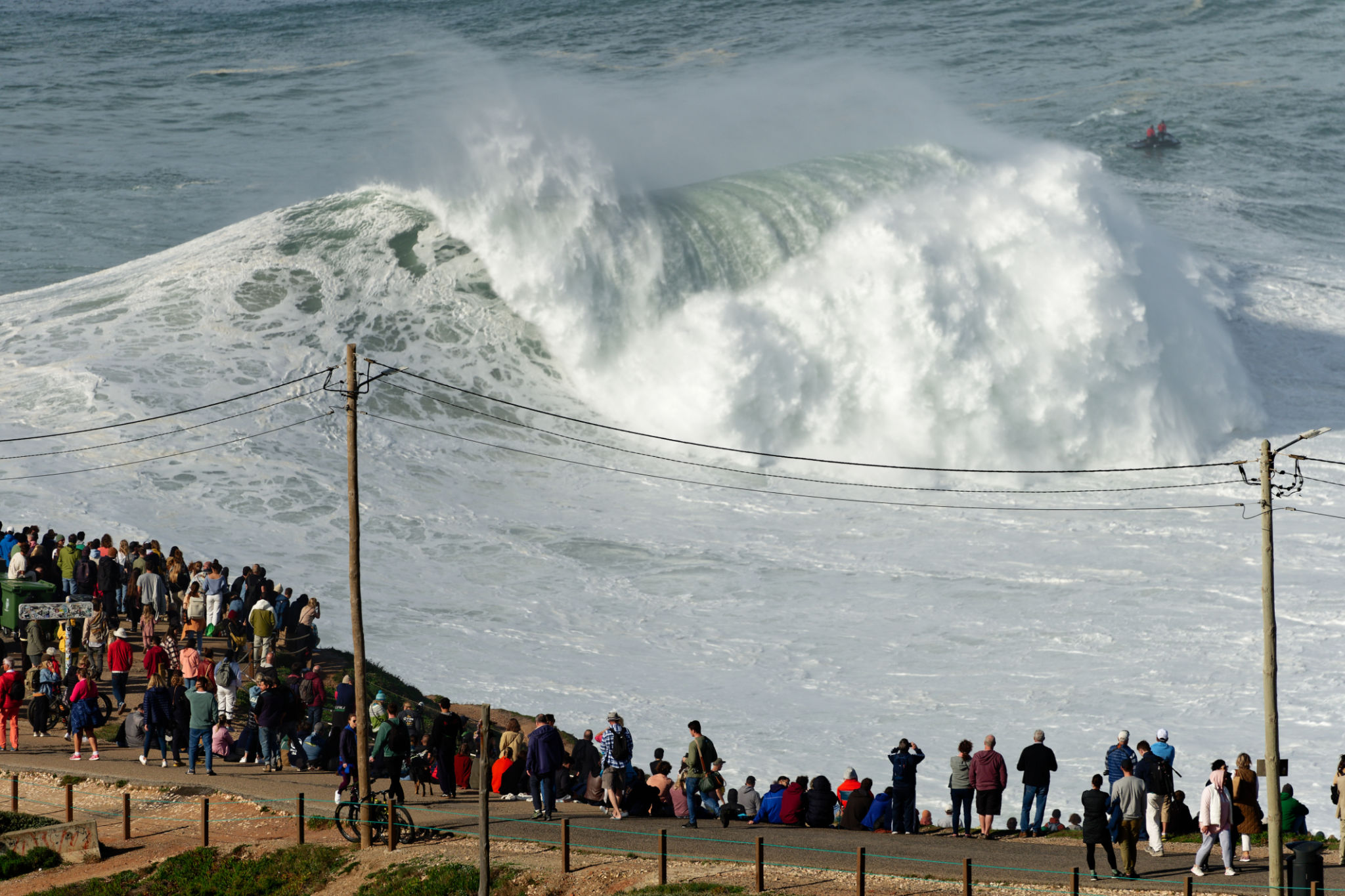 People watching the big giant waves crashing near the Fort of Nazare Lighthouse in Nazare, Portugal. Biggest waves in the world. Touristic destination for surfing. Amazing destinations. Nazare Canyon People watching the big giant waves crashing near the Fort of Nazare Lighthouse in Nazare, Portugal. Biggest waves in the world. Touristic destination for surfing. Amazing destinations. Nazare Canyon