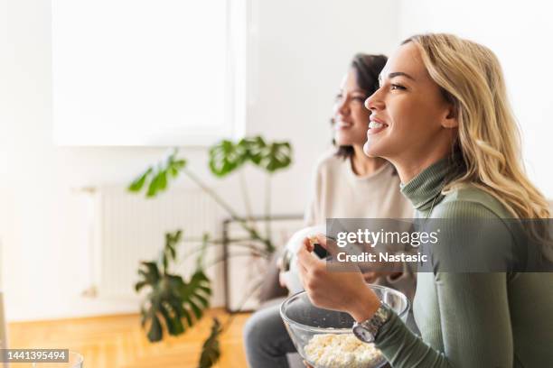 zwei junge frauen, die popcorn essen, schauen sich ein spiel im fernsehen an und jubeln - girlfriends films stock-fotos und bilder