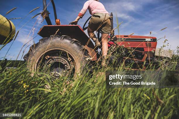 female farmer climbing on tractor in field - agricultural activity stock-fotos und bilder